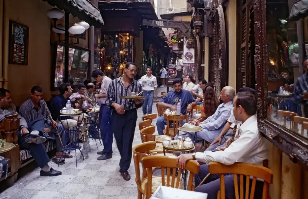 A bustling cafe in Cairo, filled with people enjoying tea, coffee, and shisha