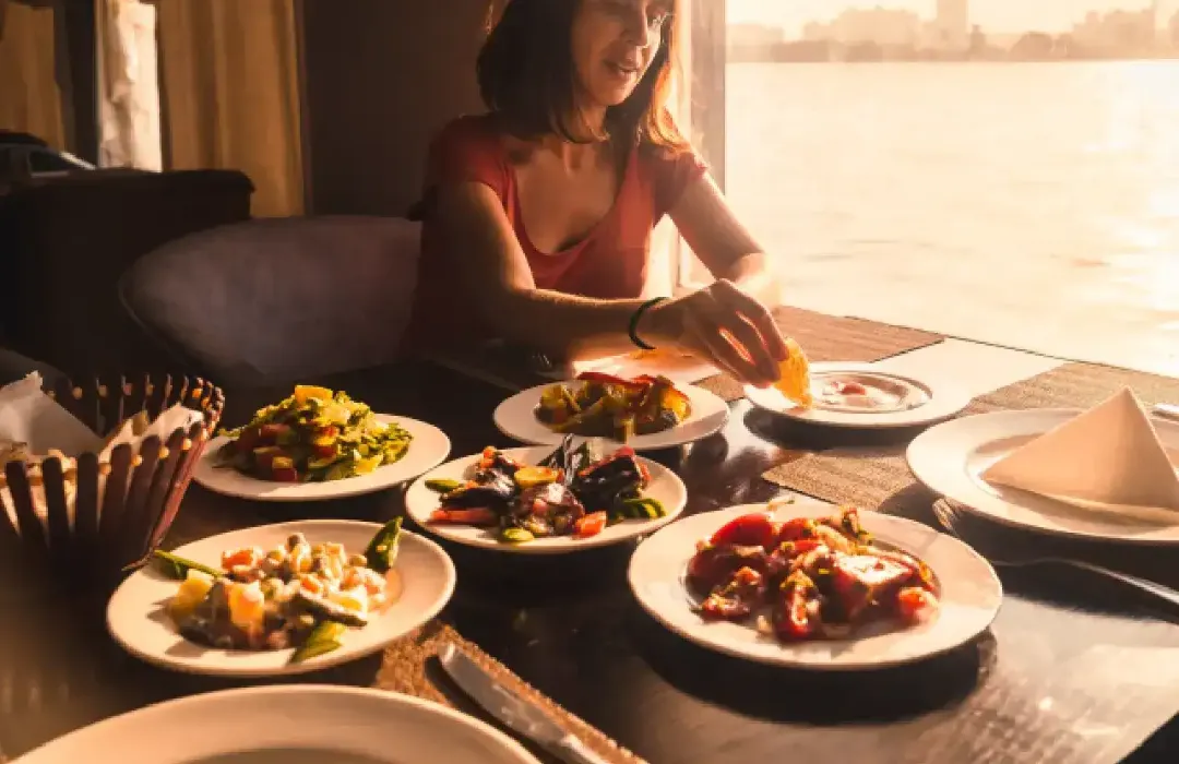 A woman savoring a meal on a boat as the sun sets over the Nile River