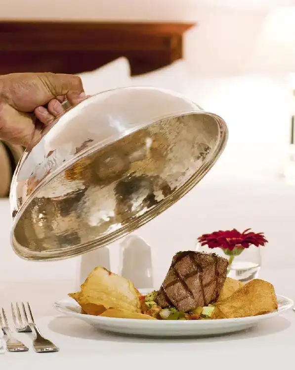 A plate of food being served under a silver cloche